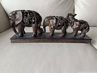 Three carved decorative elephants on rectangular base on light sofa.