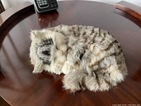 Lifelike decorative fake sleeping kitten curled up on a wooden surface showing detailed fur and facial features from side angle.