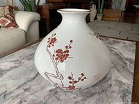 Photo showing the front and side view of the white ceramic vase with red blossom painting on the side and brown rim detail.