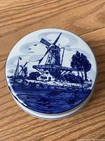 Closed view of round ceramic covered pot with blue and white hand painted Dutch windmill scene on lid.