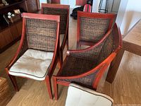 Four wooden dining chairs grouped closely together showing front rattan panel with cream cushions on some seats.