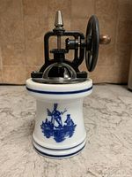 Front view of manual grinder showing ceramic base with blue painted windmill and metal grinding mechanism with turning wheel