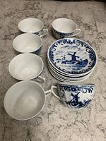 Set of six porcelain teacups and six matching saucers arranged on a countertop, showing the blue and white windmill design on the open tops and saucers.