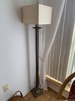 Full view of the floor lamp showing the lamp's metal base, slender pole, and square shade.
