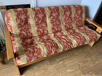 Front view of futon with striped floral upholstery and pine wood frame on a wood floor.