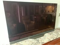 Front view of TV on stand with screen off showing bezel and speaker bar