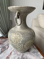 Front and angle view of ornate metal vase showing the wide neck, floral designs, and ring handle detail.