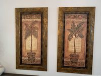 Pair of framed palm tree prints hanging on wall, showing full framed artwork of potted palm trees in botanical style.