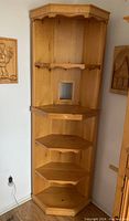 Full view of the pine corner shelving unit showing four triangular shelves with one small drawer handle and rectangular cutout for wires.