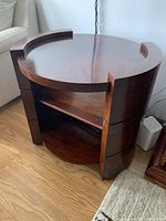 Side angle view of the round wooden side table showing the glossy finish and middle shelf with some wear.