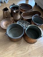 Full view of ten assorted copper pots and pieces arranged on wood floor.
