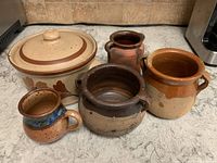 Five clay containers arranged on a countertop showing varied sizes and styles.