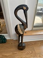 Front-left side view of the wooden carved heron showing curved neck, painted feathers, and standing on a circular base.