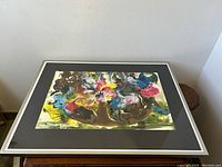 Frontal view of framed abstract painting showing vibrant mixed media shapes on black mat in silver metal frame