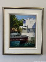 Frontal view of the framed oil painting showing dock scene and cottage with artist signature.