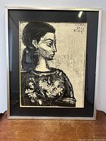 Framed vintage art print of a woman in profile with floral corsage, black matting and silver frame, standing on a wooden surface.