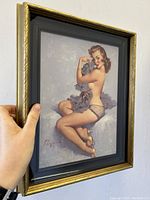 Side angle view showing the framed Elvgren pin-up print 'Roxanne'. The gold frame and black inner mat are visible.