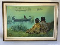 Frontal view of large framed painting featuring two Indigenous natives seated by water with fishing canoes and artist signature visible.