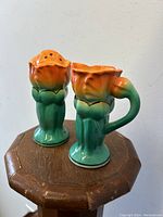 Pair of Japanese Art Deco lustre ware sugar shaker and creamer jug, floral design in orange and green, displayed on wooden surface