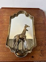 Full front view of the brass mirror and giraffe sculpture on wooden surface
