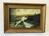 Frontal view of the framed oil painting showing a river landscape with trees and hills under a partly cloudy sky, artist signature 'GM' visible in the lower left corner.