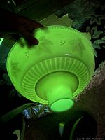 Glass shade held under black light showing bright green uranium glass fluorescence