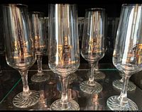 Group of six clear champagne flutes with gold Olympic embellishments and swirl bases