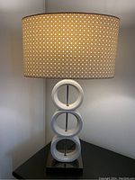 Full view of lamp showing circular ring white base and beige lampshade with white circular hole pattern.
