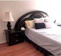 Photo showing black lacquer queen size headboard attached to two matching end tables with metallic drawer handles and matching lamp on one side of the bed.