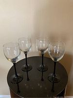 Four black lacquer stem wine glasses arranged upright on black surface