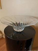 Side angle view of a large clear crystal bowl with flared rim and swirl pattern on the base, placed on a black round surface.