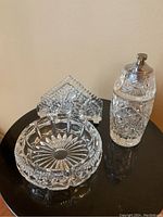 Crystal lighter, ashtray, and napkin holder arranged on black surface, showing the starburst cut-glass pattern on each item.