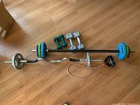 Top view of exercise equipment set showing barbells, dumbbells, weight plates and resistance band on wooden floor.