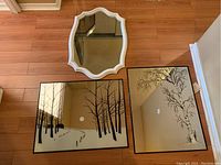 Top-down photo of three mirrors: two rectangular etched mirrors with tree designs and one antique scalloped white framed mirror.