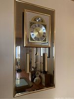Full view of the rectangular brass framed Tempus Fugit wall clock with glass front, showcasing the clock face with Roman numerals, hanging weights, and pendulum.