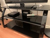 Full front view of Bello black glass TV stand holding electronic devices on the shelves