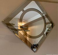 Square two-tone smoke and clear mirror hung wall-mounted diagonally, showing circular pattern in center and reflection of room.