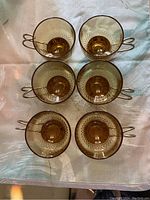 Top view of six amber glass espresso cups arranged on a fabric surface showing their translucent amber glass and metal loop handles.