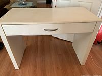Front view of white wooden desk showing one drawer with metal handle.