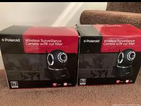 Two boxed Polaroid Wireless Surveillance Cameras with IR cut filter IP300B shown side by side on carpeted stairs.