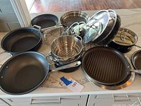 Overview of all nonstick pans, grill pan, steamer basket, lids and rack arranged on countertop