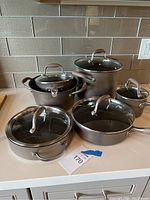 Five hard-anodized pans and pots on countertop with lids