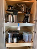 Cabinet shelf showing Breville toaster oven, electric coffee pot, drip coffee machine, stovetop coffee pot, and clear plastic container