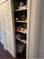 Wide view of closet shelves showing stacked board games, textiles like pillows, boxes, bags and candles on multiple shelves.