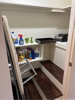 Ironing board leaning against wall with shelves holding various cleaning supplies such as sprays and bleach.