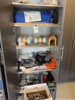 Full view inside cabinet showing blue camping gear bag, plastic Easter eggs, small house decoration, clothing, jars, and containers.