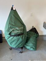 Two green fabric storage bags, one covering tree on wheeled base and one standalone bag