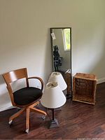 Full view of lot items arranged on wooden floor against wall: chair, two lamps, mirror, wicker basket