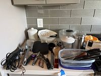 Full view of kitchen counter with multiple kitchen utensils, gadgets, and storage containers laid out.