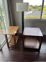 Photo showing the wooden floor lamp and two side tables by a window on dark wood flooring.